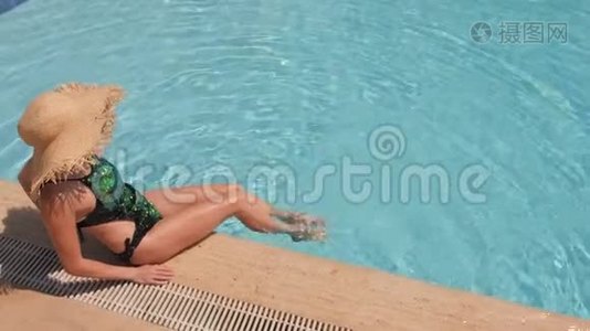 一个戴着草帽的女人在蓝色的游泳池里放松。 俯视图，慢动作视频