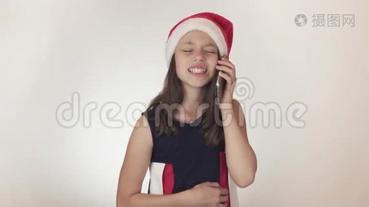 戴着圣诞老人帽子的漂亮顽皮少女在白色背景下的智能手机上进行情感交流视频