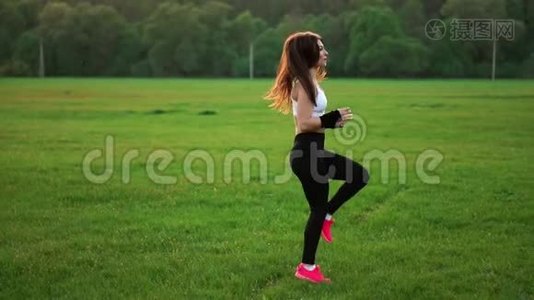 日落时分，在草地上一个运动的女孩，穿着白色的上衣和粉红色的运动鞋，在提起前进行热身运动视频