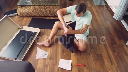 一个年轻人在他家的客厅里独立收集家具。一个男人收集一张电脑桌。视频
