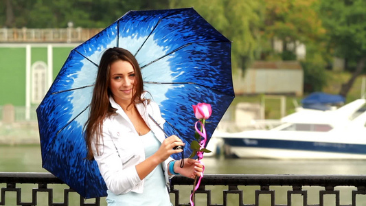 美丽的女孩在水边手拿玫瑰撑着雨伞拍摄视频