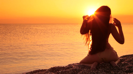 一个年轻女人坐在海滩上闪闪发光的轮廓视频
