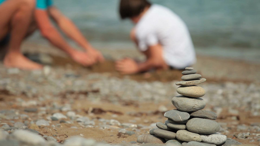 父子在夏天的海滩上建造沙堡在前景平衡的石头上视频