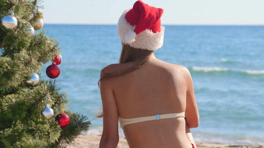 戴着圣诞老人帽的比基尼女孩坐在海滩边视频