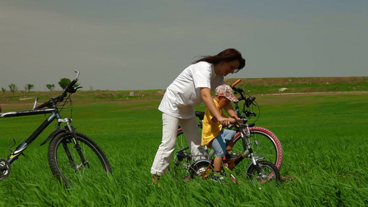 母亲在麦田里教蹒跚学步的孩子骑自行车视频