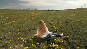 金发女孩坐在开满黄色花朵的草地上22秒视频