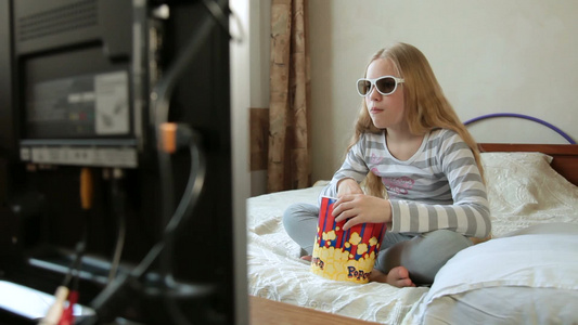 戴着眼镜的金发女孩坐在床上吃爆米花看电影视频