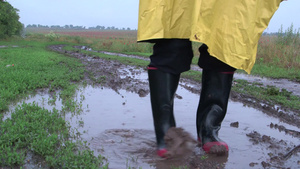 穿雨衣男子在乡间路上的水坑里洗去橡胶靴上的污垢15秒视频
