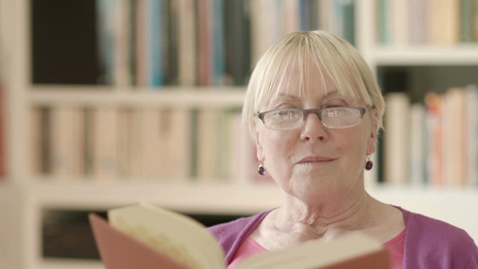 快乐的退休妇女戴着眼镜在家看书[永远快乐]视频