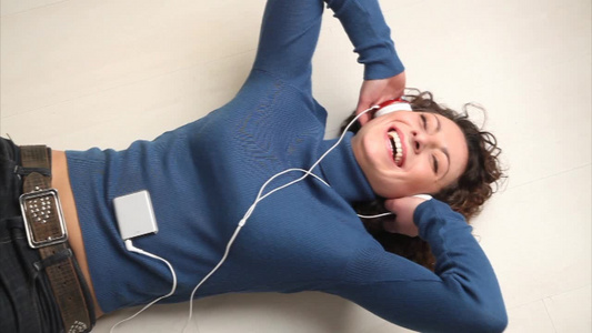 年轻的女人躺在地板上听音乐视频