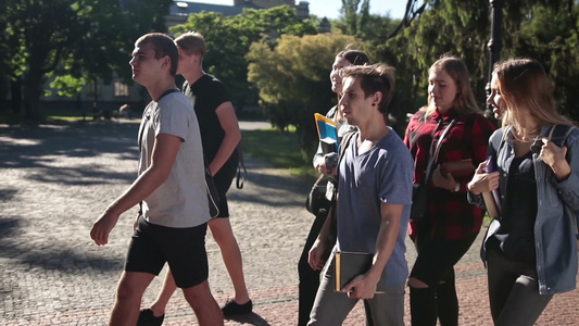 一群活泼阳光的大学生带着背包和书籍走在大学校园视频