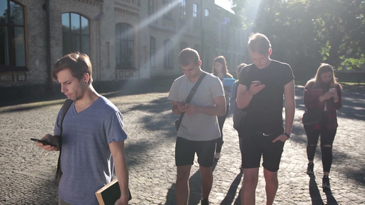一群时髦的大学朋友在大学校园里一起散步时用手机浏览网络视频