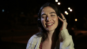 夜晚在路灯下黑发女孩戴着耳机跟着耳机里的音乐在唱歌17秒视频