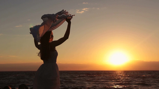 女孩拿着飞舞的丝巾站在海边视频