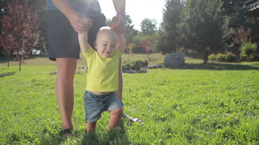 父亲帮助可爱的男孩在草坪上蹒跚学步视频