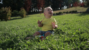 可爱的小婴儿坐在绿色的草地上微笑着拍手慢15秒视频