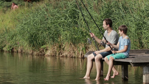 中年男子和男孩在湖边坐在木墩上钓鱼39秒视频