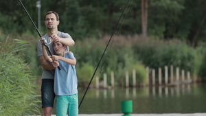 十几岁的孩子在父亲的帮助下在池塘里学习如何用旋转棒和卷轴钓鱼29秒视频