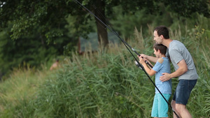 一对父子在夏天的湖边钓鱼儿子抓住了一条鱼爸爸试图帮助儿子12秒视频
