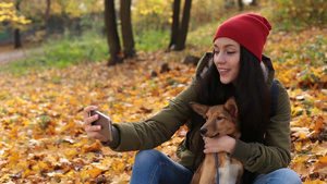女人和她的狗在彩色秋天公园用智能手机上自拍18秒视频