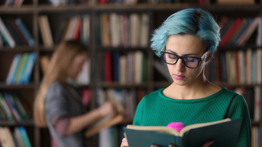 戴着眼镜的蓝发女大学生全神贯注地在大学图书馆看书视频