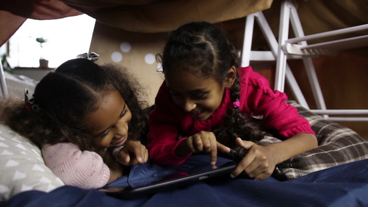 快乐的混合种族两个小女孩在数字平板电脑上观看有趣的视频，视频