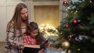 漂亮的年轻母亲在圣诞树附近给她可爱的女儿读书12秒视频