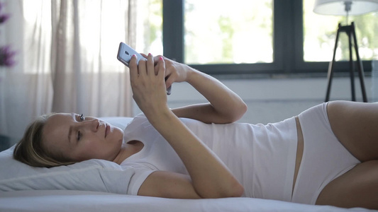 清晨年轻女性躺在床上浏览手机视频