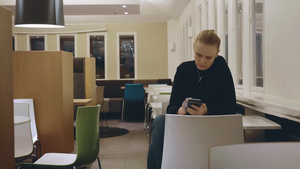 金发女人坐在空咖啡馆的桌子上用智能手机阅读17秒视频