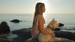 小女孩和它的宠物狗坐在海边的石头上看日落14秒视频