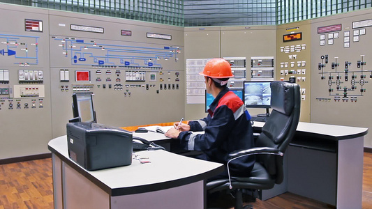 工程师坐在煤气压缩机站主控制面板前面的桌子边记录注册表视频