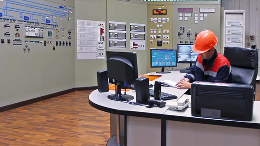 工程师坐在桌子前在气体压缩机站的主控制面板附近写注册表视频