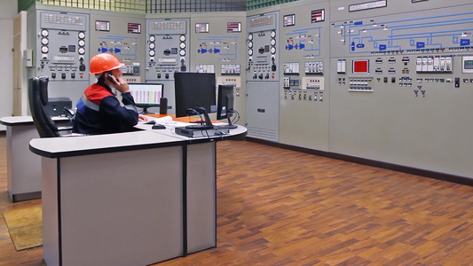 工程师坐在压缩机站主控制面板前打电话交谈视频