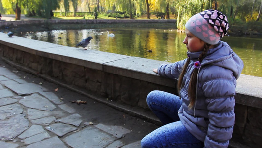 可爱的女孩在秋天城市公园里拿着爆米花喂鸽子视频