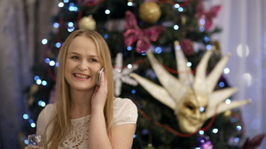 在圣诞节美丽的金发年轻女子微笑着喝着香槟一边用手机说话24秒视频