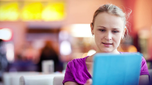 年轻的女人在咖啡馆里用她的平板电脑视频