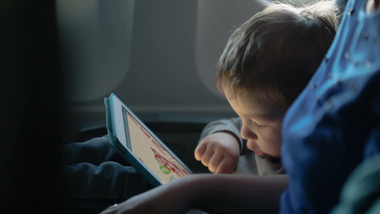 小男孩坐在飞机上玩一台平板电脑视频