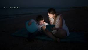 妈妈和她的小儿子晚上在海滩上玩触控板10秒视频