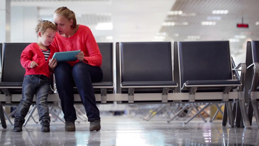 年轻的母亲和儿子在机场候机楼坐在候机室里玩平板电脑视频