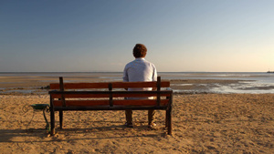 孤独的年轻人坐在海滩上的长凳上22秒视频
