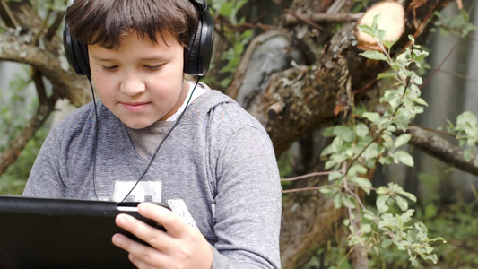 青少年在户外戴着耳机使用平板电脑视频