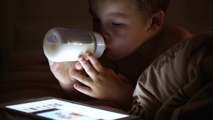 床上的小男孩从瓶子里喝牛奶同时看着平板电脑11秒视频