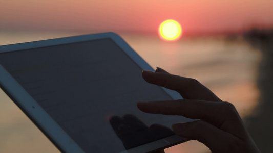 特写镜头女性的手在平板电脑上打字背景是日落在海上视频