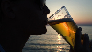 日落时一位戴太阳镜的年轻女子在海滩上喝啤酒13秒视频