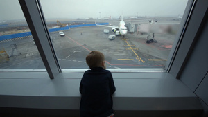 好奇的小男孩在登机时站在窗口看着窗外的机场16秒视频