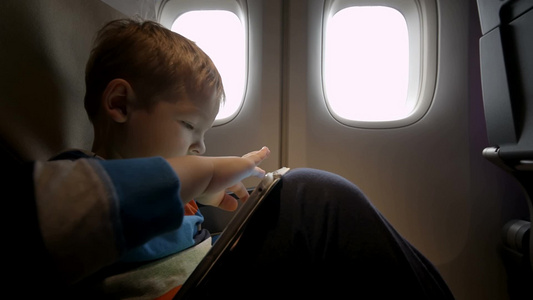 小男孩坐在飞机上玩平板电脑视频