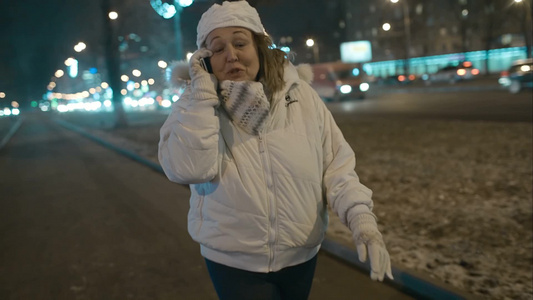 在寒冷的晚上一个妇女在街上一边散步一边打电话视频