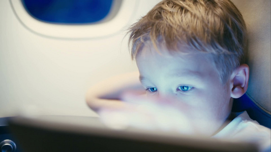 一个小男孩在飞机上玩触摸板的特写镜头孩子看起来累或无聊视频