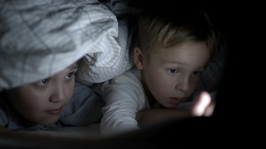 两个男孩晚上躺在床上的毯子下在触摸板上看卡通或电影29秒视频
