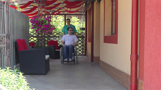 女护士推着坐在轮椅上推着坐在男病人到户外行走视频